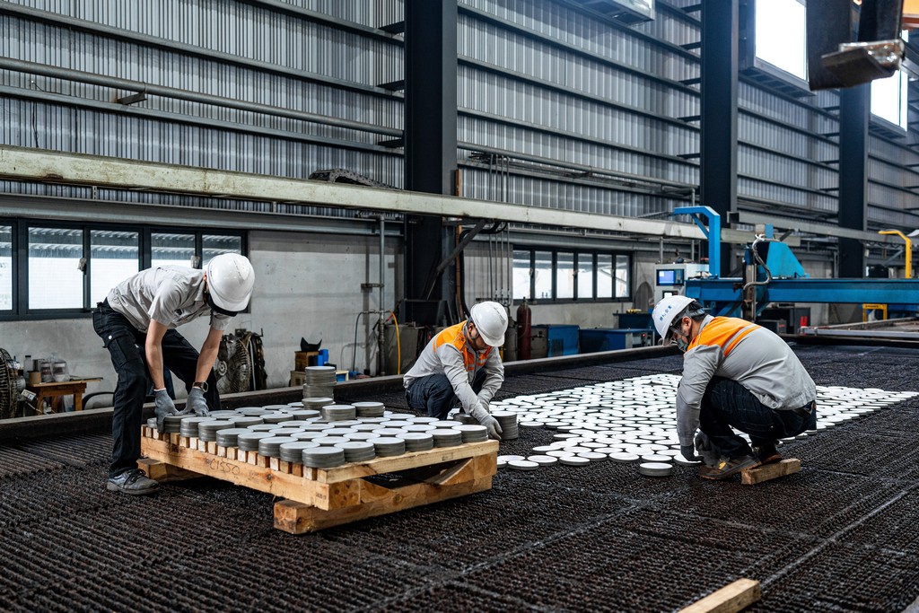 三名工人正在切割機旁整理和堆疊圓形金屬墊片。