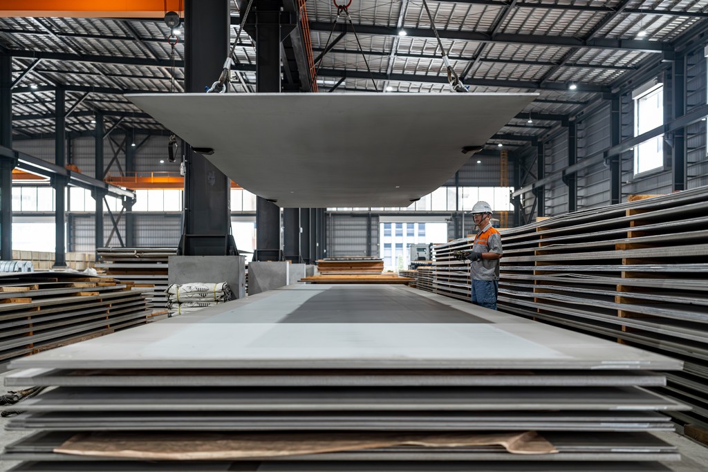 佩戴安全帽的技術人員操作天車吊運大型金屬鋼板。