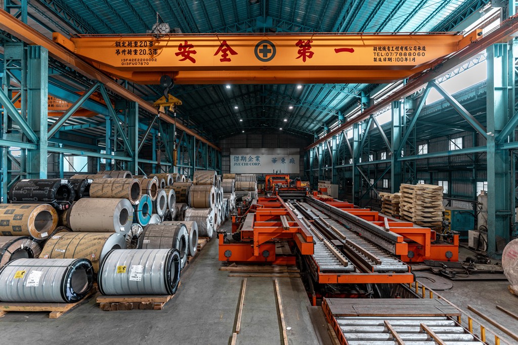 鋼捲庫存與生產線全景，天車標語「安全第一」。