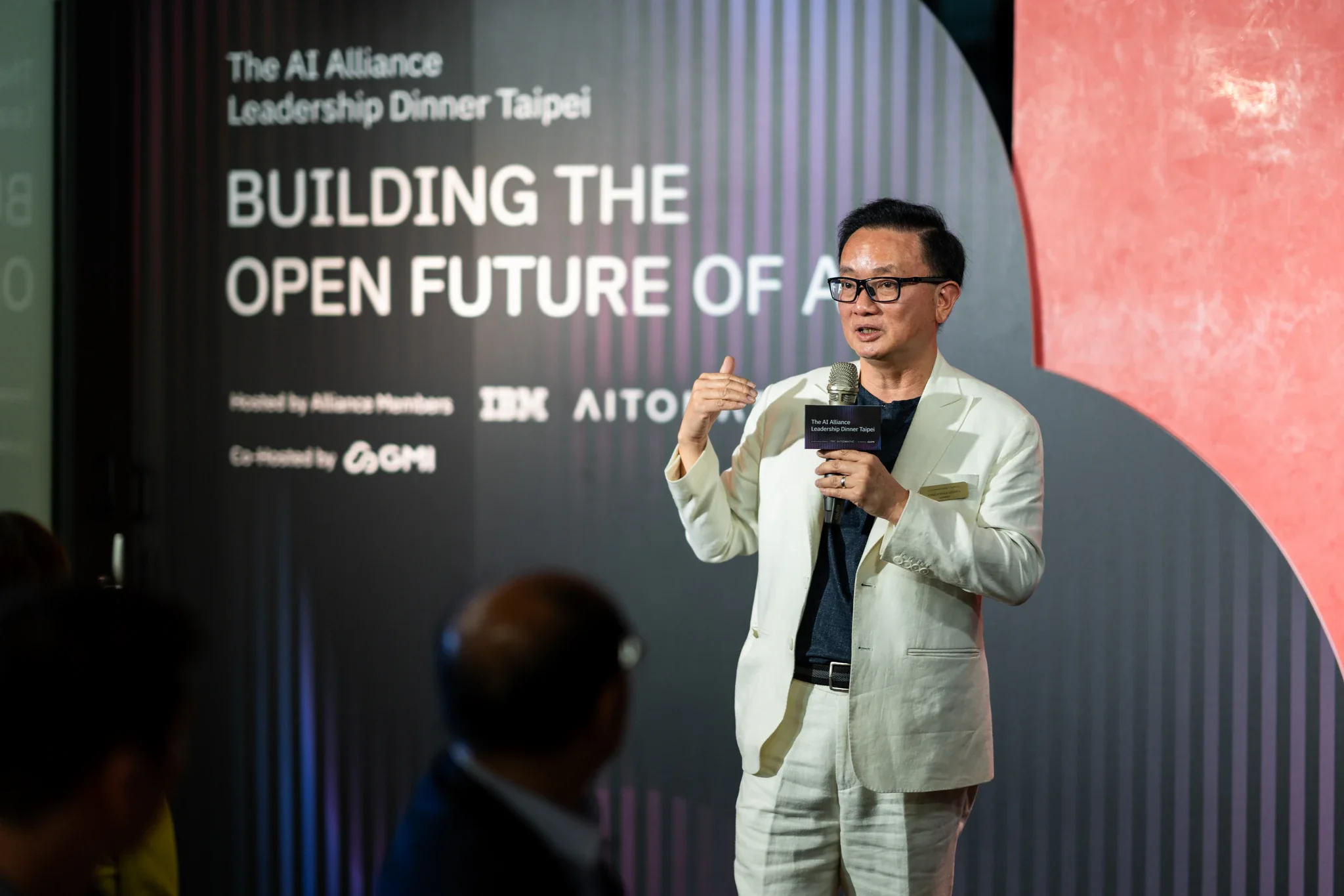 AI Alliance 科技領袖交流|主題背板與講者 穿淺色外套的講者站在 AI Alliance 主題背板前發言