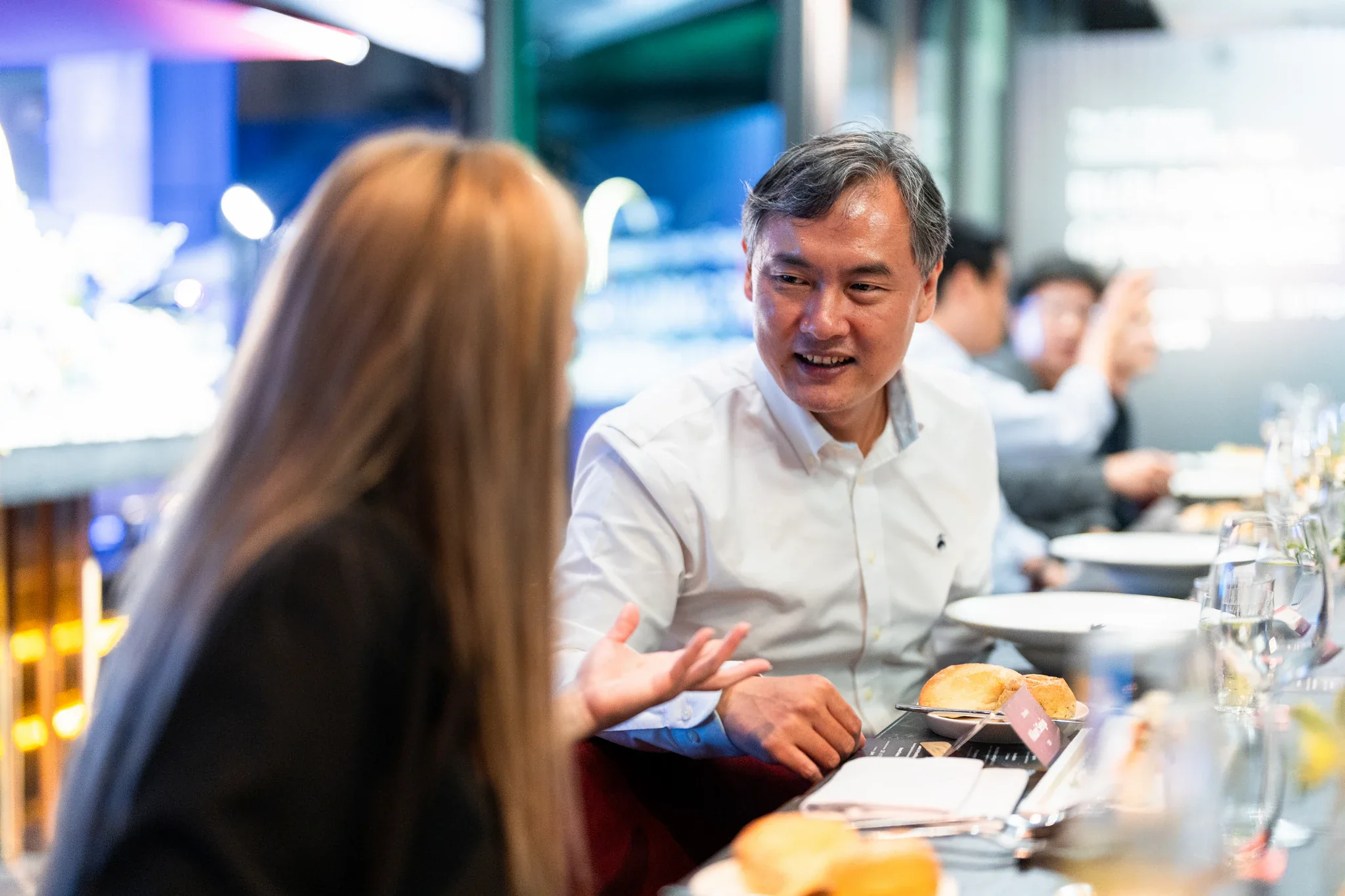 AI Alliance 領袖晚宴|賓客餐敘 晚宴中一名男士與對座來賓交談,桌面有餐盤與酒杯