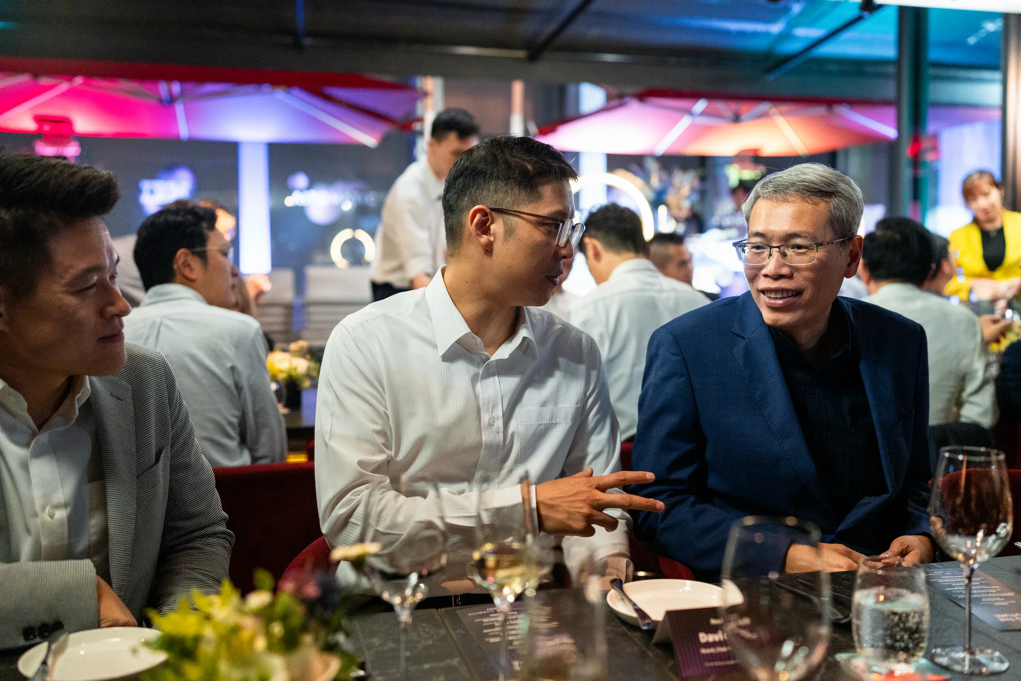 台北企業晚宴攝影|餐桌自然互動 兩位男士在晚宴餐桌前笑著交談,現場可見用餐布置
