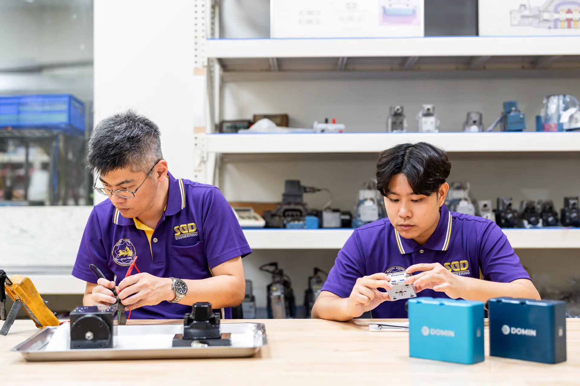 協聚德技術團隊|桌上零件檢視 兩名協聚德員工坐在工作檯前,專注檢視桌上的小型零件與裝置