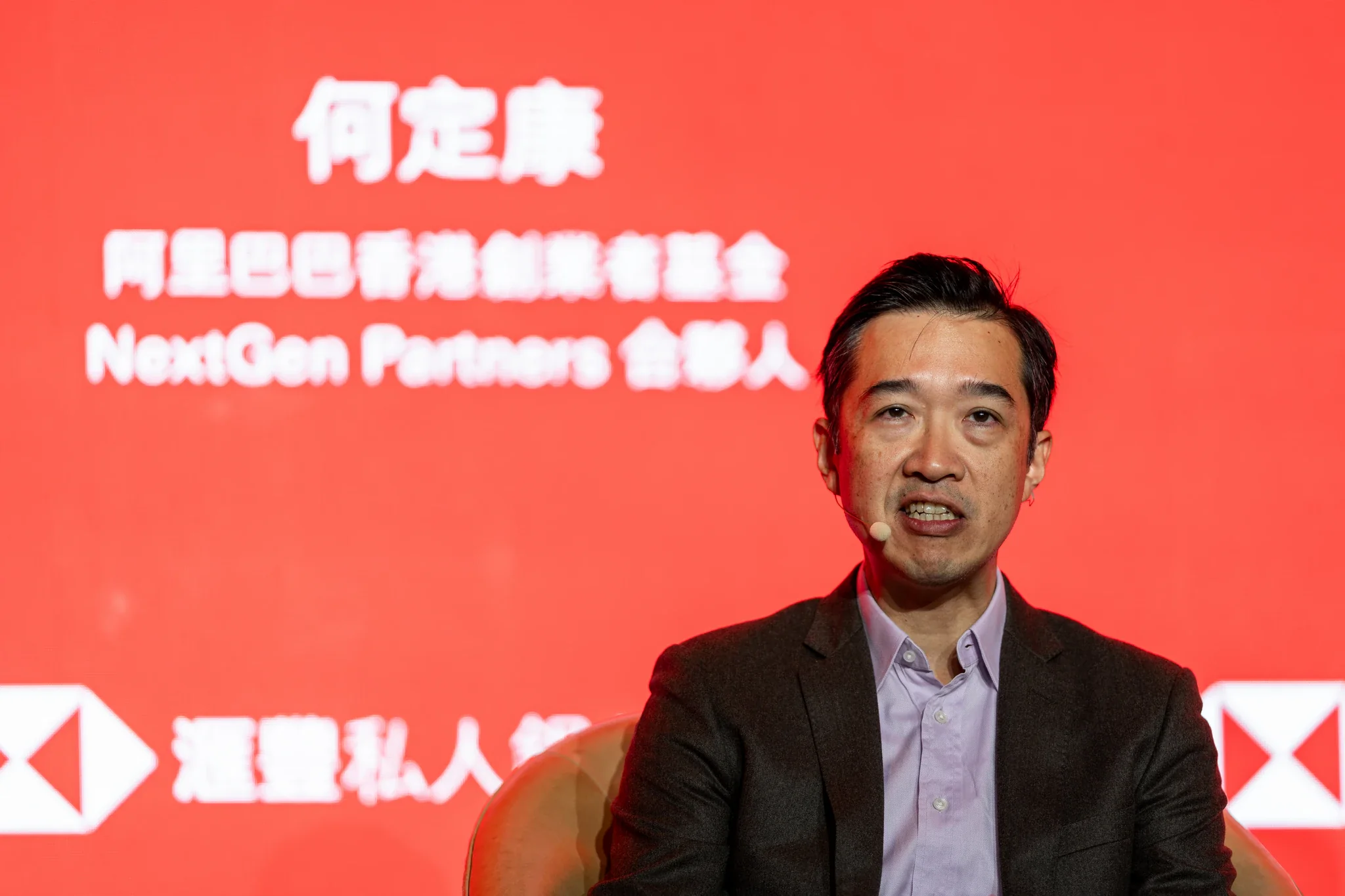 HSBC 金融論壇|座談嘉賓特寫 一名男士在紅色滙豐主題背板前參與座談發言