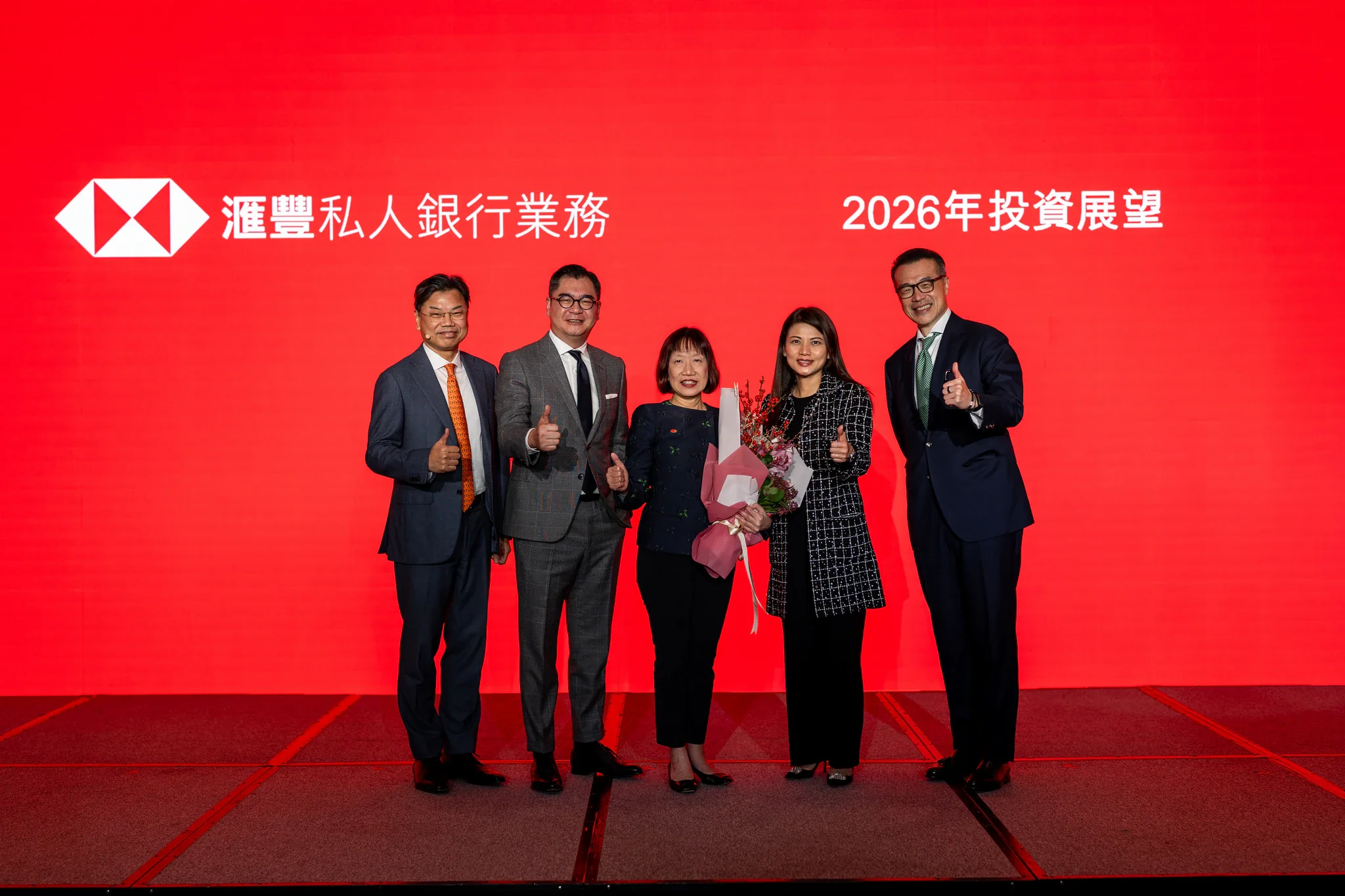 滙豐銀行 2026 投資展望|講者團體合影 五名參與者在印有 HSBC 標誌的紅色舞台背景前合照