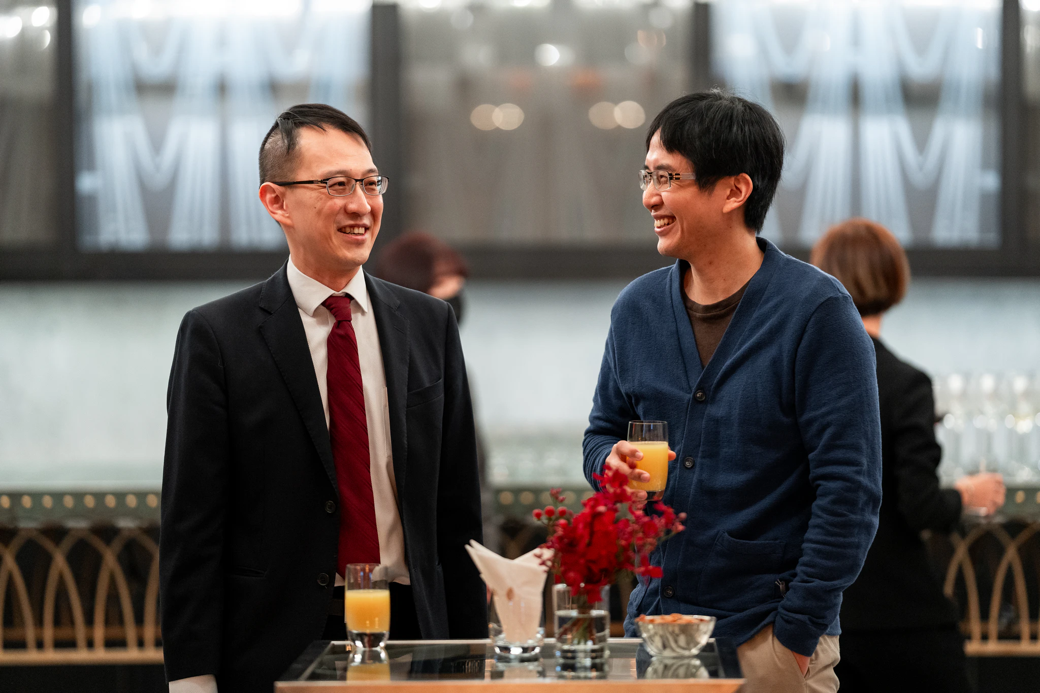 滙豐銀行活動攝影|會場來賓交流 兩位男賓客在宴會場地的桌旁微笑交談,桌上可見紅色花藝裝飾