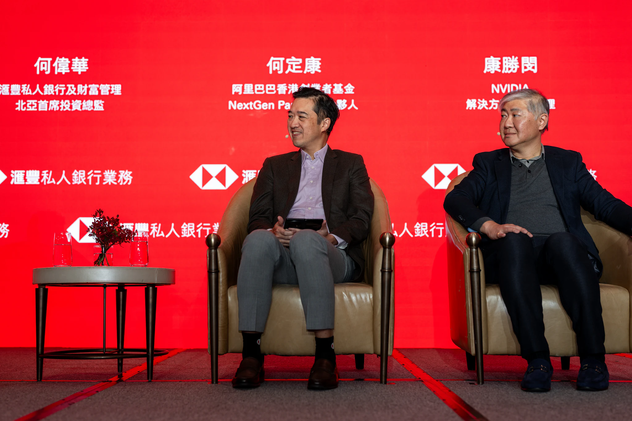 HSBC 台北金融論壇|兩位座談嘉賓 兩位男與談者坐在滙豐銀行紅色主視覺舞台的扶手椅上,背後可見品牌標誌